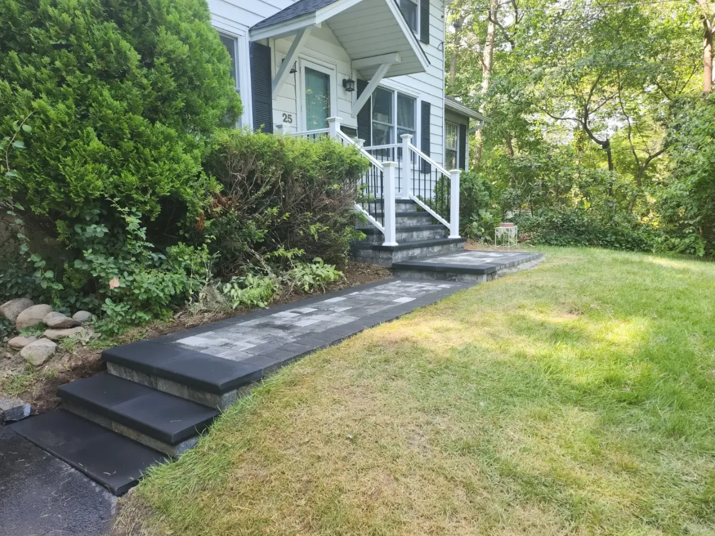 Paver walkway and steps leading to a front stoop with white railings, by Promaster Maintenance Corp
