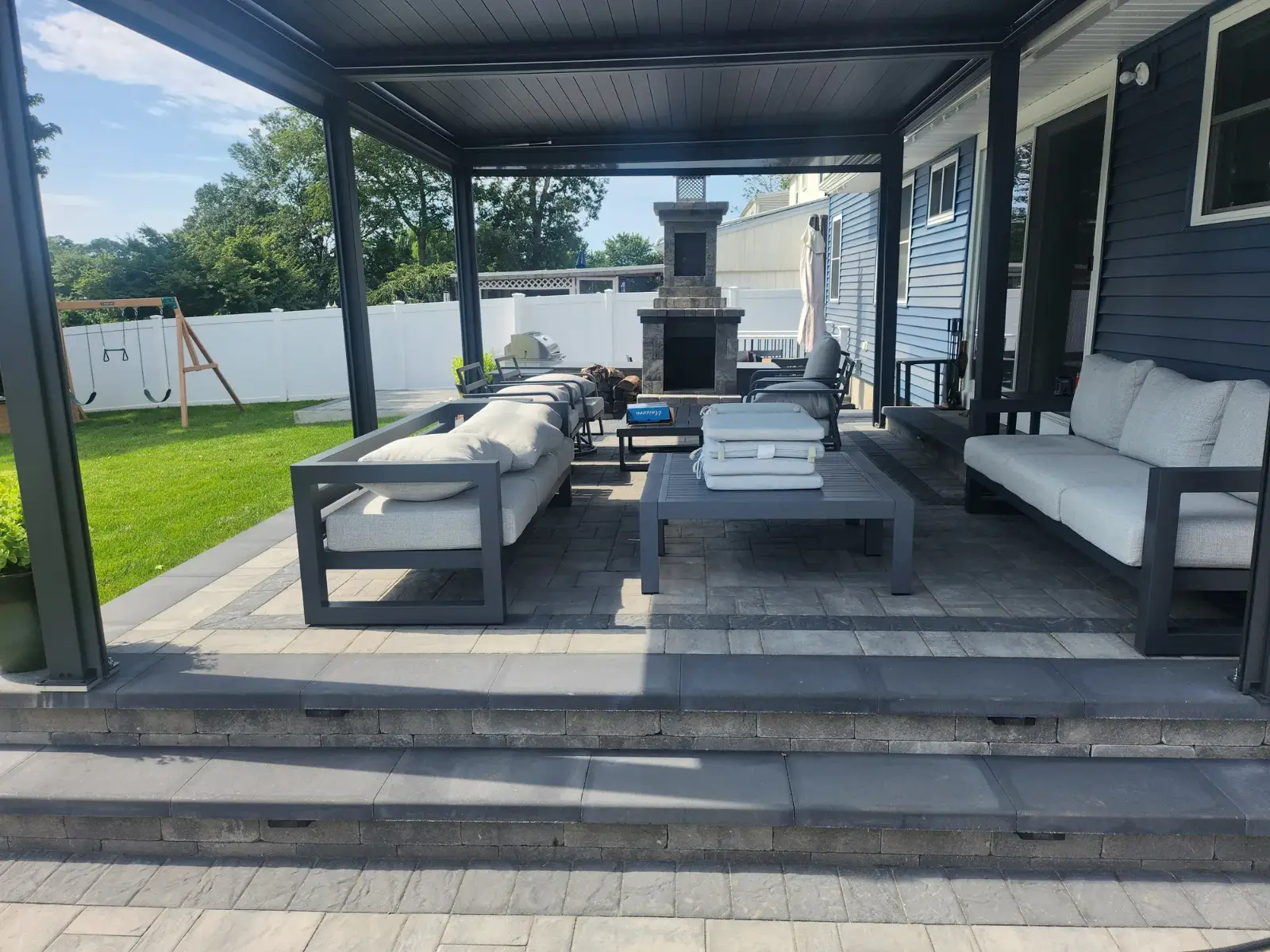 Covered paver patio with stone outdoor fireplace, seat-wall steps and lounge area by Promaster Maintenance Corp, Long Island